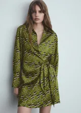 Vestido corto de tejido fluido color verde con estampado abstracto en blanco y negro. Diseño cruzado con cuello camisero, mangas largas y cierre de lazo lateral.