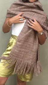 Ruana de lana merino tejida artesanalmente en telar, de color visón con diseño recto y terminación de flecos en los extremos.