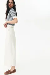 Pantalón palazzo color blanco hueso de tiro alto con elástico oculto en la cintura, cierre lateral oculto y pinzas que realzan la figura. Modelo de corte holgado con bolsillos al bies, bolsillos decorativos atrás y piernas tres cuartos con raya adelante y atrás.