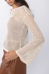 Top de tejido calado color marrón con mangas largas acampanadas y detalle de broches decorativos en el escote.