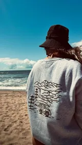 Buzo gris con cuello redondo y puños y cintura acanalados. Estampado en la espalda con diseño de montañas, árboles, río y camioneta.