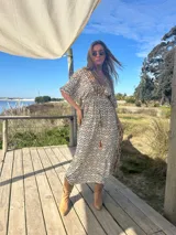 Vestido largo de seda color crema con estampado geométrico en tonos camel y negro. Tiene escote en V, mangas cortas amplias y cintura ajustable con cordón.