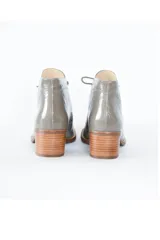 Botín gris de cuero charol brillante, con cordones frontales y tacón bloque de madera clara de 6 cm.