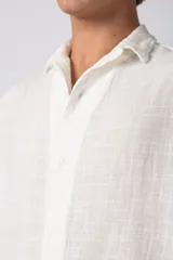 Camisa de lino color blanco, de manga corta, con cuello clásico y cierre frontal con botones.