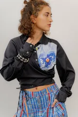 Camisa crop negra con estampado de una flor y un insecto, con cintas para atar en la cintura.