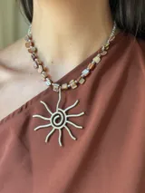 Collar corto con cuentas de nácar y dije de sol plateado hecho a mano en alpaca. Se cierra con cadena de acero quirúrgico y ganchito para regular el largo.