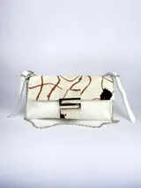 Cartera bandolera color gris con solapa de pelo blanco con estampado de círculos marrones. Cierre con botón magnético y herraje metálico plateado en forma de "S".
