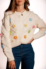 Saco de punto color rojo, con cuello polo y cierre frontal de botones blancos. Presenta flores bordadas en relieve de diferentes colores (azul, amarillo, verde, naranja, rosado) y mangas largas con diseño de burbujas.