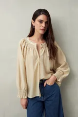 Camisa color crema de lino con cuello redondo, canesú fruncido, mangas largas amplias con puños elastizados con volado y cierre frontal con botones.
