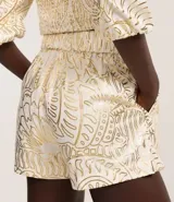Short de cintura alta color crema con estampado abstracto dorado, cintura elástica y superposición delantera.