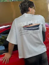 Remera amarilla de corte holgado con estampado trasero de un yate y texto con nombres de ciudades.