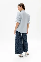 Blusa de lino color rojo con volados frontales que enmarcan el pecho, cuello redondo con mini volado y mangas 3/4 abullonadas con puño elástico. Presenta un cierre frontal con botones y una silueta relajada.