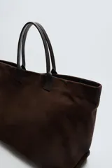 Bolso tipo shopper marrón oscuro, fabricado en cuero con acabado serraje. Tiene un compartimento principal con cierre magnético y un bolsillo interior con cremallera. Cuenta con dos asas de mano de cuero.