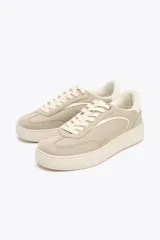 Zapatillas deportivas color beige, estilo soft, con cuerpo en combinación de materiales y cierre mediante cordones. Suela de 3 cm de altura.