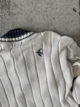 Buzo tejido verde con escote en V, cuello con rayas blancas y azul marino, y puños y ruedo con detalle de rayas.