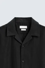 Camisa color marrón oscuro de corte relaxed fit, confeccionada en tejido de lino. Tiene cuello bowling, manga corta, bajo con aberturas laterales y cierre frontal de botonadura.