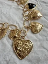 Collar dorado con doble cadena, una de eslabones grandes y otra de eslabones pequeños, con múltiples dijes de corazones dorados y negros.