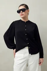 Camisa color marrón claro con cuello mao, mangas 3/4 abullonadas y cierre frontal con botones. Presenta pequeños pliegues en los hombros y detalle calado sutil.