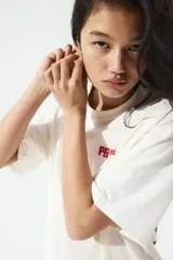 Remera blanca de corte amplio con cuello redondo y mangas cortas. Estampado pequeño con la palabra "PACHA" en rojo en el lado izquierdo del pecho.