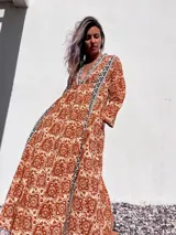 Túnica larga de color beige con estampado floral en tonos terracota y detalles geométricos en negro y blanco en el escote y a lo largo del frente.