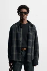 Camisa de hombre regular fit confeccionada en tejido de algodón a cuadros en tonos azul oscuro y verde oliva. Tiene cuello solapa, manga larga con puños abotonados, bolsillo de plastrón en el pecho y cierre frontal con botones.