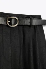 Pantalón negro de tiro alto con pinzas delanteras, pernera ancha y cinturón de cuero con hebilla dorada.