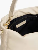 Cartera bombonera color crema con asa corta y correa larga extraíble. Tiene cierre con cordón ajustable y detalles metálicos dorados.