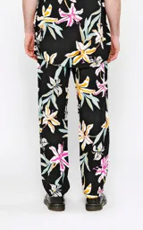 Pantalón recto unisex con estampado floral en tonos rosa, amarillo, celeste y blanco sobre fondo negro. Confeccionado en rayón.