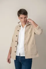 Sobre camisa color beige confeccionada en lino, de corte recto, con cuello clásico, manga larga con puños abotonados, cierre frontal con botones a tono, bolsillo de parche en el pecho y ruedo recto.