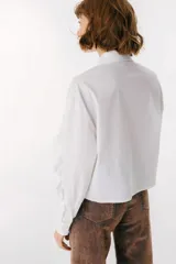 Camisa celeste con cuello clásico, cierre frontal con botones y mangas largas con volados.