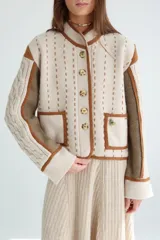 Chaqueta corta de lana color negro con detalles en beige y marrón. Tiene cuello mao, cierre frontal con botones y bolsillos de parche.