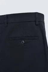 Pantalón chino color beige, de corte recto y tiro medio. Confeccionado en tejido de algodón con elasticidad, con bolsillos laterales y traseros de vivo. Cierre frontal con cremallera y botón.