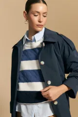 Trench color beige de corte clásico con cuello amplio, botones frontales, detalles en los hombros y mangas largas.