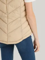Chaleco acolchado Tommy Hilfiger color beige con capucha ajustable con cordones y cierre de cremallera frontal. Cuenta con bolsillos laterales con cremallera y detalles distintivos de la marca.