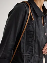 Camisa negra de lino con corte femenino, cuello clásico, cierre frontal con botones y mangas 3/4 con puños enrollados. Presenta detalles de frunces verticales en el frente y bolsillos de parche a la altura de la cadera.