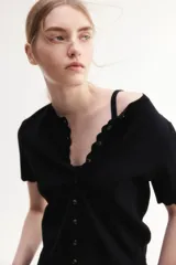 Saco corto negro de punto fino suave con cuello redondo, mangas cortas y botonadura frontal. Tiene ribete festoneado en tapeta, mangas y bajo.