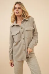 Camisa estilo leñador color beige con textura de espiga, de manga larga con puños abotonados, cuello clásico, cierre frontal con botones y dos bolsillos de parche con solapa abotonada en el pecho.