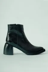 Bota corta de cuero negro, con caña media y punta cuadrada. Se caracteriza por su taco geométrico y voluminoso, con acabado texturado.