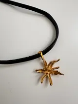 Gargantilla de cuero negro con dije dorado en forma de flor.