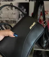 Bandolera negra de cuero sintético con correa regulable y logo plateado.