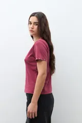 Remera de manga corta color bordó con cuello redondo y pequeños ojalillos metálicos decorativos en los bordes de las mangas.