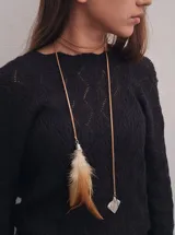 Gargantilla de cuero color beige con dije de pluma marrón y blanca y dije de cristal transparente.