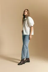 Camisa blanca de manga corta con volumen en los hombros, cuello camisero y cierre frontal con botones dorados.