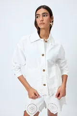 Sobrecamisa blanca de algodón con cuello camisero, botones marrones y detalles de encaje calado en el ruedo.
