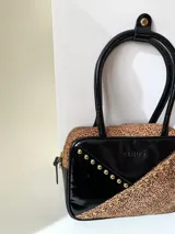 Cartera rígida negra de cuero con tachas plateadas y tres combinaciones de cuero diferentes que aportan textura. Tiene herrajes y cierre metálico plateado marca YKK. Cuenta con un asa fina para llevar al hombro o en la mano y una correa larga extra regulable.