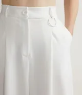 Pantalón largo de vestir color blanco, de corte palazzo, con pliegues frontales, bolsillos laterales y detalle de anilla metálica en la cintura.