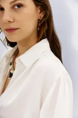 Camisa blanca de manga larga confeccionada en viscosa con acabado sandwash, de textura suave y aterciopelada. Cuello camisero con botón en forma de corazón y frunces en el canesú delantero y la espalda.