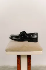 Mocasín de cuero color marrón con tachas metálicas plateadas en la puntera y laterales.