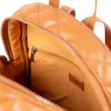 Mochila color habano con diseño acolchado en símil cuero, costuras a tono y herrajes plateados. Tiene acceso con cierre, dos compartimentos, un bolsillo interno con cierre y dos abiertos. La correa es regulable y el interior es de tela de algodón y poliéster.