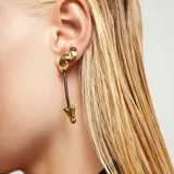 Pendientes largos dorados con poste de tuerca. Consisten en una pieza superior ovalada dorada, un cordón negro y un dije inferior con forma de corazón tridimensional.